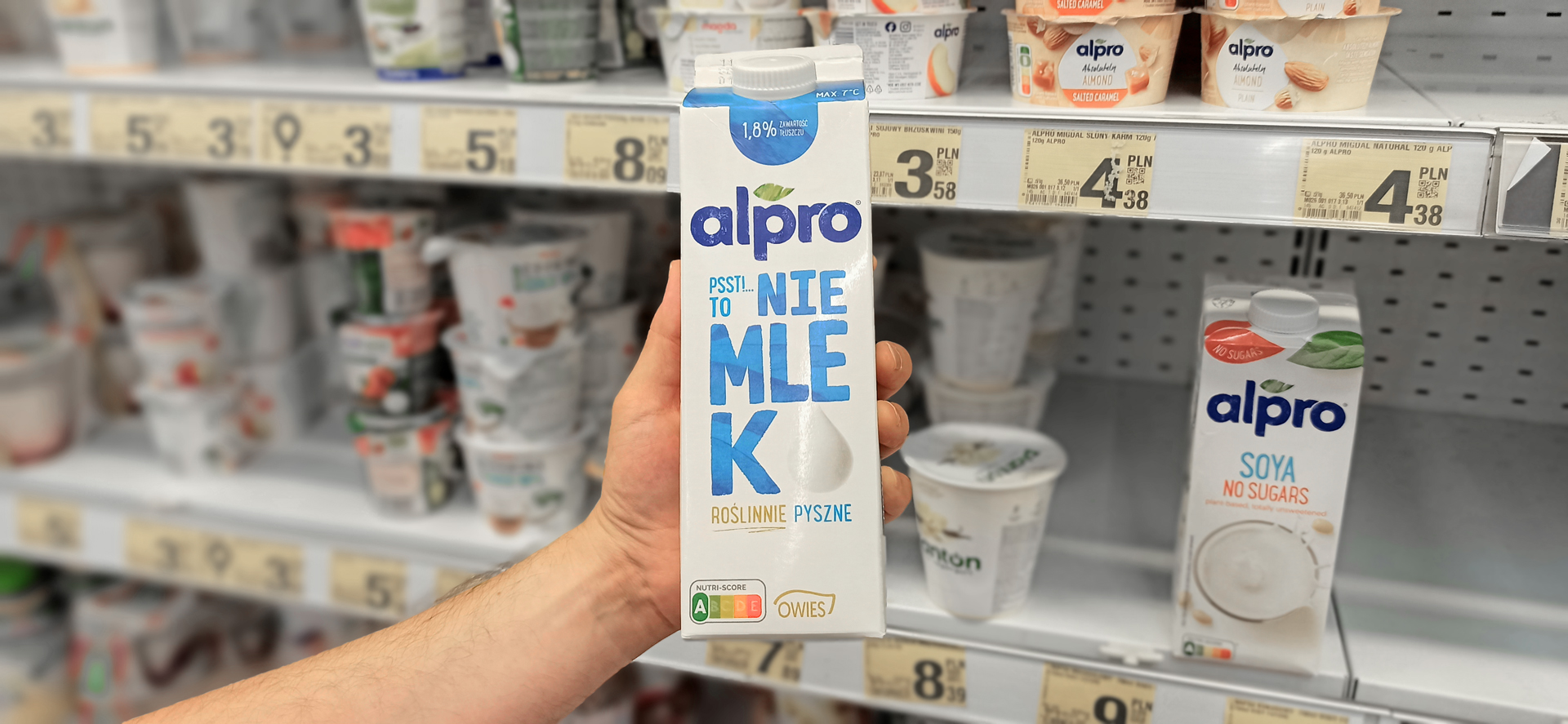 Alpro plant-based milk packaging held by one hand and supermarket shelves in the background